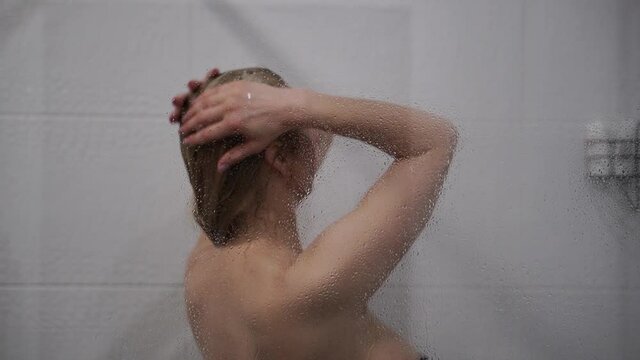 Woman washing hair behind glass of shower stall