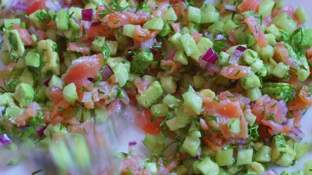 Preparation of tartar salad with smoked salmon, avocado, cucumber, onions and dill.