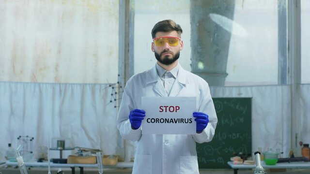 In front of the camera scientist man in the biotechnology lab holding a poster with the Stop Coronavirus he looking straight to the camera concept of COVID-19