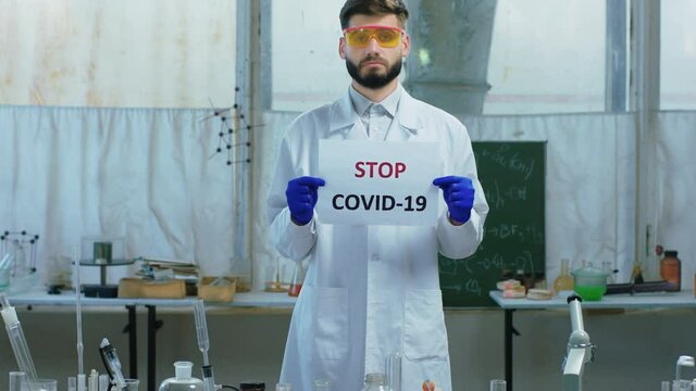 In a biochemical laboratory scientist man holding a poster with Stop Covid he are concentrated looking straight to the camera concept of COVID-19
