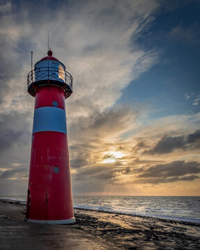 Red and white striped lighthouse in front of clouded sunset sky at the shore of Westkappelle in the Netherlands