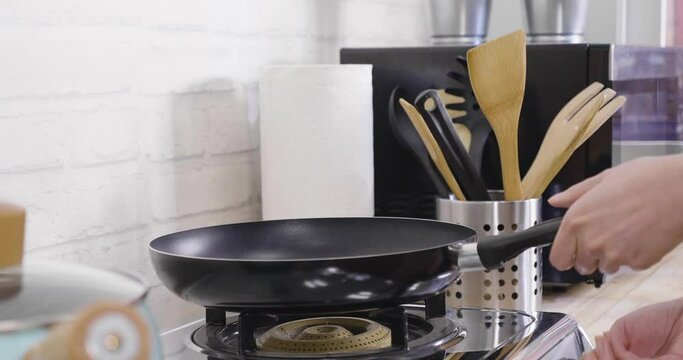 Slow motion close up shot of asian lady turning on stove under cast iron skillet pan in kitchen. woman hands switch button to turn on fire to heat the frying cooking tool at home indoors.
