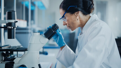 Medical Development Laboratory: Female Scientist Looking Under Microscope, Analyzes Petri Dish Sample. Specialists Working on Medicine, Biotechnology Research in Advanced Pharma Lab. Close-up Shot.