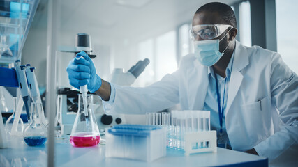 Medical Development Laboratory: Black Scientist wearing Face Mask Uses Pipette for Filling Test...