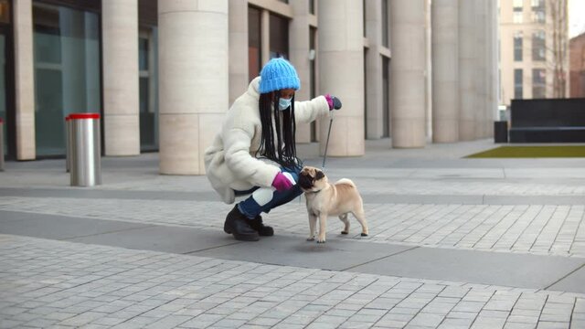 African woman in mask spraying detergent after pet peeing on sidewalk outdoors