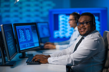 Fototapeta premium Call-center worker is speaking with the client by headset. Workplace of the african-american support operator.