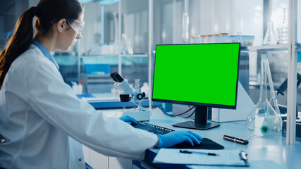 Medical Science Laboratory: Microbiologist Working on Computer with Display with Green Chroma Key Screen. Diverse Multi-Ethnic Team of Biotechnology Scientists Developing Drugs.
