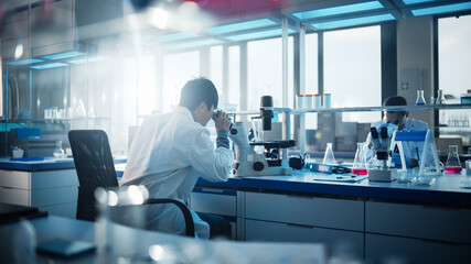 Medical Development Laboratory: Scientist Looking Under Microscope, Analyzes Petri Dish Sample. In...