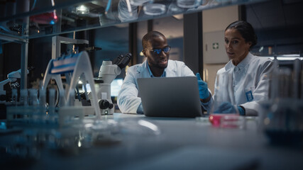 Modern Medical Research Laboratory: Caucasian and Black Scientists Work on Laptop, Do Data...