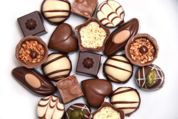 election of luxury chocolates, with a variety of shapes including a heart, florentines, and pistachios. White, milk and dark chocolate and could be for a gift. They are against a white background.