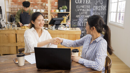 Smiling asian woman shaking hands to mortgage insurance broker at cafe meeting. happy lady handshaking with sales consultant making deal. male waiter prepare meal of customer order in counter.