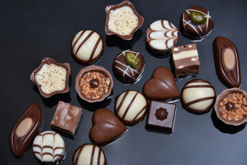 Selection of luxury chocolates, with a variety of shapes including a heart, florentines, and pistachios. White, milk and dark chocolate and could be for a gift, black background.