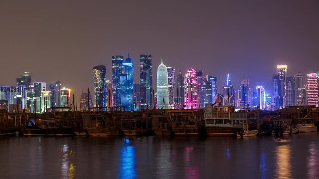 A panoramic view of the old dhow harbour night timelapse in Doha, Qatar, with the West Bay skyline in the background. Modern skyscrapers on background and old boats on foreground.