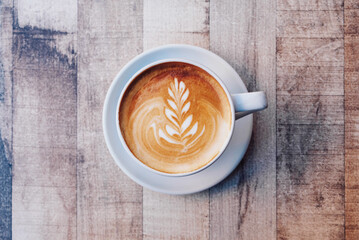 A cup of fresh delicious italian cappuccino coffee with latte art in the shape of leaf on wooden...