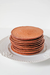 Freshly cooked soft delicious gluten free protein chocolate pancakes stacked on white plate, close up. Space for text. Healthy sweet food.