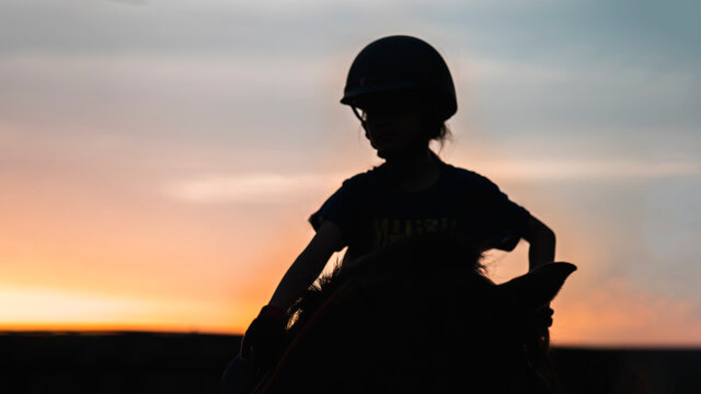 Silhouette image of school kid girl riding horse againts the twilight sky.