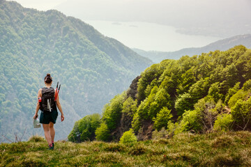 Fototapeta na wymiar Girl hiker with backpack and trekking poles walk along a mountain path with a man on the hand in a sunny day. on the background the lake Maggiore, Val Grande National Park, Europe, Piedmont Italy.