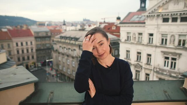 Portrait of a cheerful woman posing against the backdrop of the roofs of the old city, hands hair. Preparing a journalist for an interview.