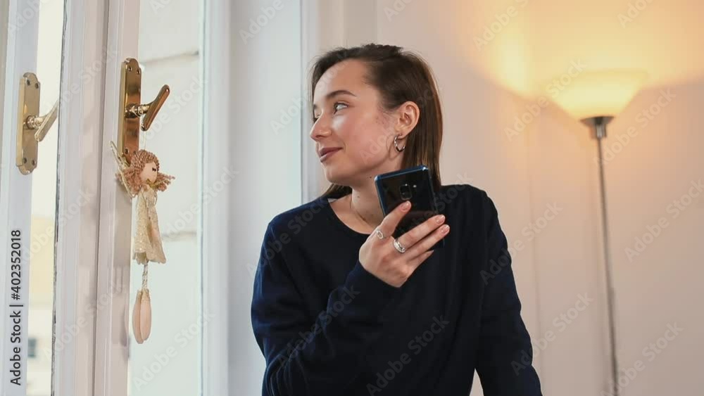 Poster the woman uses the phone in her hands near the window. writes a message by clicking on the screen. l