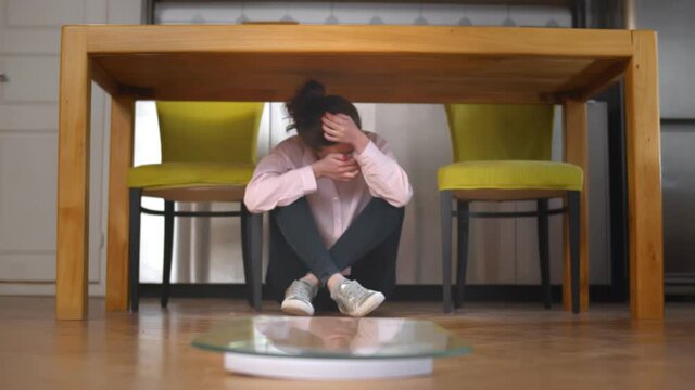 Young stressed woman obsessed with diet sitting under table at home with scales on foreground