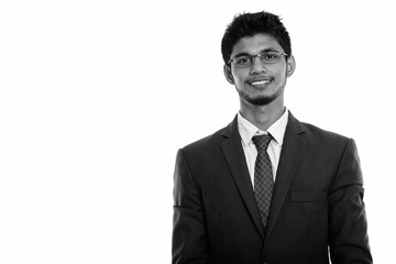Studio shot of young happy Indian businessman smiling while wearing eyeglasses