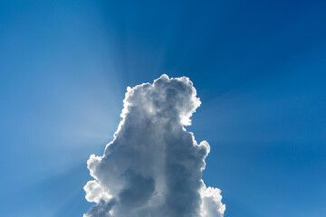Cloud on a background of blue sky, behind the cloud the sun's rays shine.
