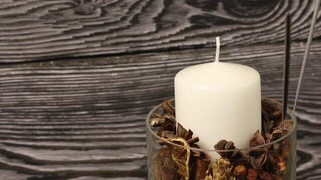 A candle in a glass candlestick with pine cones, dried fruits and sparklers. Rotates against the background of black pine boards.