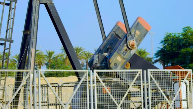 Close-up of oil pump working against palm trees and blue sky
