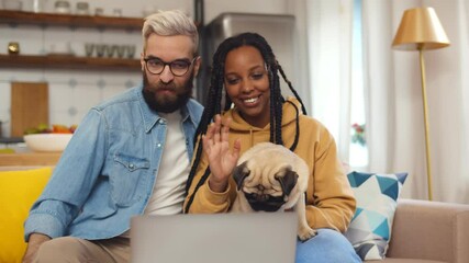 Happy multiethnic couple relax with dog on couch and having video call on laptop