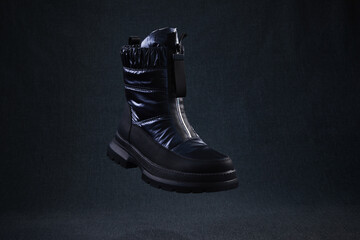 Fashion black unbranded boot flying on dark background. Black winter walking shoes levitate in air....