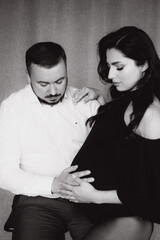 Pregnancy photo session in a photo studio with a fabric background in a black bodysuit and tights
