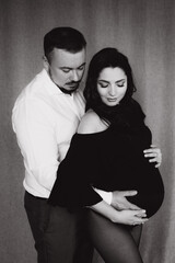 Pregnancy photo session in a photo studio with a fabric background in a black bodysuit and tights
