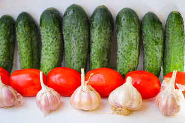 Several green cucumbers and red tomatoes and garlic  are stay in a rows on a white background
