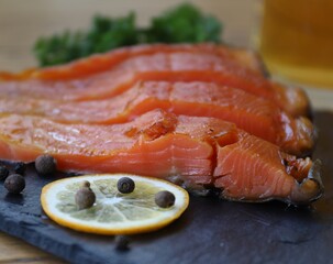 red slices of smoked sea trout lie on a black basalt board next to a slice of lemon and spices without people