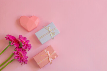 Happy Mothers Day, Womens Day, Valentines Day or Birthday. Gerbera, gift and heart on a pink background. Floral flat lay with beautiful real greeting card. Copy space.
