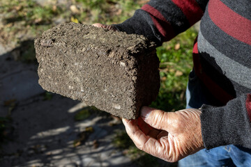 A man holds in his hand a building block made of peat and excipients.