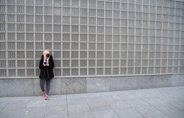 Mujer rubia con mascarilla negra mirando el teléfono móvil en un fondo de cuadrados de cristal .