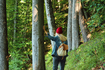 Naklejka na ściany i meble A woman traveler walks through the forest. Beautiful nature landscape in woods. Hiking journey on tourist trail. Outdoor adventure. Travel and exploration. Healthy lifestyle, leisure activities