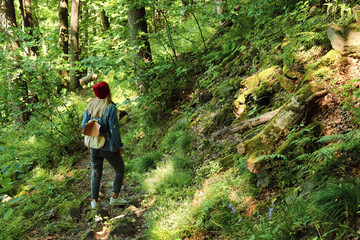 Obraz premium A woman traveler walks through the forest. Beautiful nature landscape in woods. Hiking journey on tourist trail. Outdoor adventure. Travel and exploration. Healthy lifestyle, leisure activities