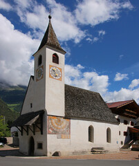 Fototapeta na wymiar Street with the small gothic village church of St Jakob and its traditional wood shingle roof in Rabland, Vinschgau region, South Tyrol in Italy