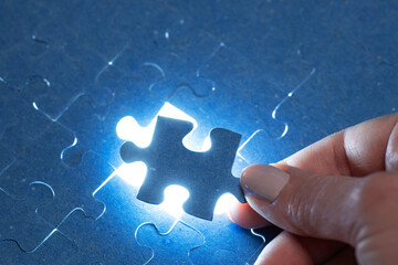 The missing piece of the puzzle with light, the concept of completing a big job, the final of the project, the successful solution of business problems. The hand puts the last piece of the jigsaw - obrazy, fototapety, plakaty