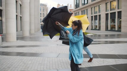 Businessman and businesswoman in coat shelter umbrella from the rain and strong wind outside