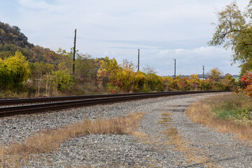 Fototapeta na wymiar Curved train tracks running through a rural area, fall landscape with autumn leaves, horizontal aspect
