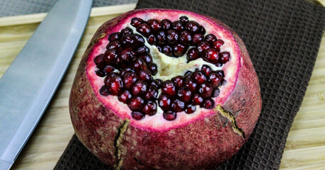 Cut off the top of the whole pomegranate platter on a napkin / cloth on a wooden tray on a blue background. Large red ripe pomegranate with a knife next to it. The concept of healthy living. Fruit.
