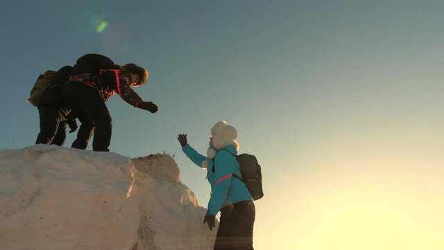 Climbers climb mountain extending a helping hand to each other. Teamwork of travelers. Happy tourists jumping and waving their hands on top of mountain. Hikers in the mountains at sunset.