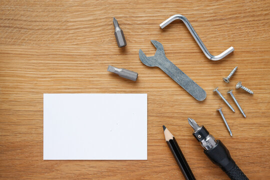 on a wooden table lies a white note, a black pencil nails, screws and screwdriver, wrench, space for text and no person