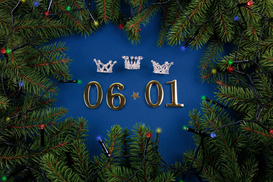 Golden numbers of January 06th and three crowns on blue background with green branches of spruces and shining garland. Happy Epiphany day, three kings day.