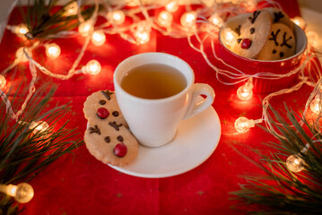 Christmas card, decor, cup of tea, gingerbread New Year's deer, candies, lights, tree on a red background