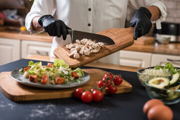 Close up of chef hands with kitchen knife cutting meat on a wooden board