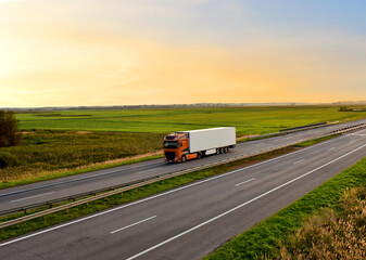 Fototapeta na wymiar Truck with semi-trailer driving along highway on the sunset background. Goods delivery by roads. Services and Transport logistics. Modern Lorry Transport concept. Long Self-driving lorries